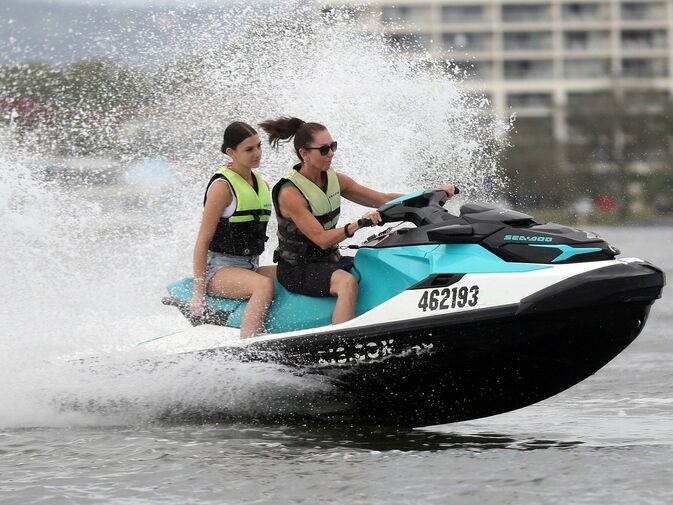 Two women ride a jet ski at high speed on open water, creating a large splash—one of the top adrenaline Gold Coast experiences for thrill-seekers.