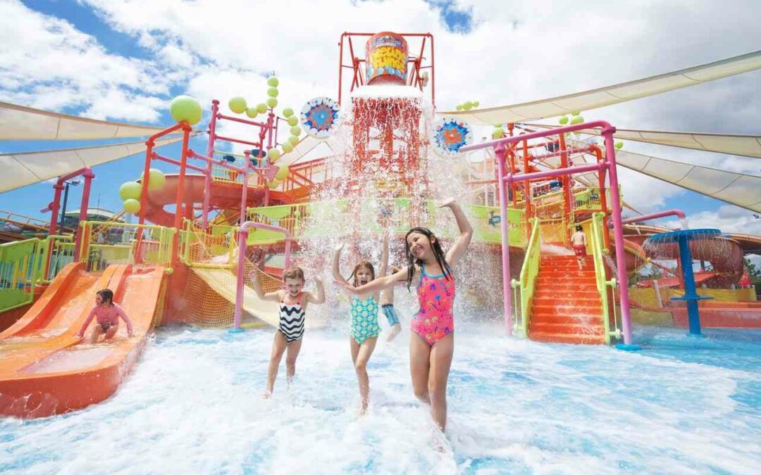 Children play and laugh under a giant tipping bucket at a colorful Gold Coast water park, featuring slides, splash zones, and family-friendly fun.
