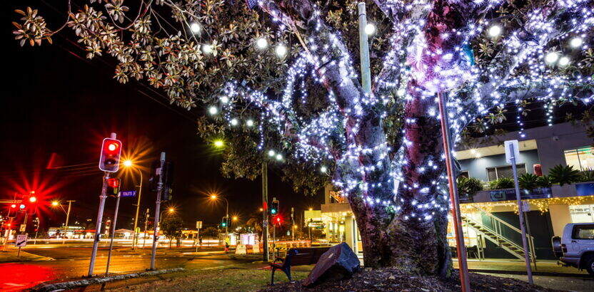 Tree decorated with bright Christmas lights along a lively street at night, showcasing the festive spirit of Gold Coast Christmas events.