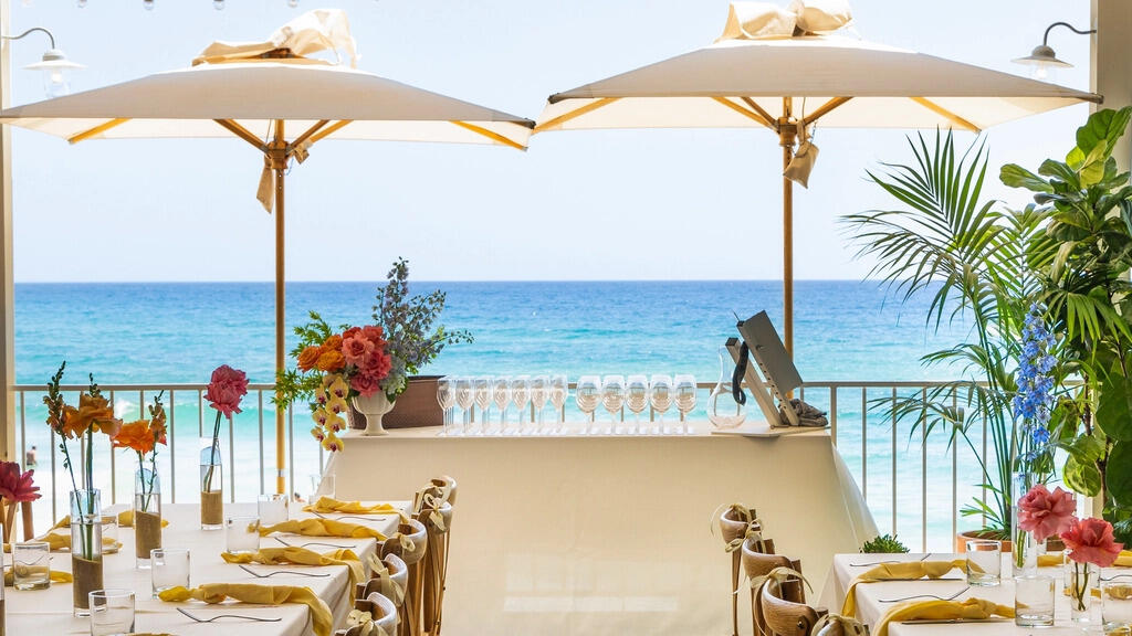 gold coast australia places to visit: beachfront dining setup at The Burleigh Pavilion with umbrellas, floral tables and an ocean view over Burleigh Beach